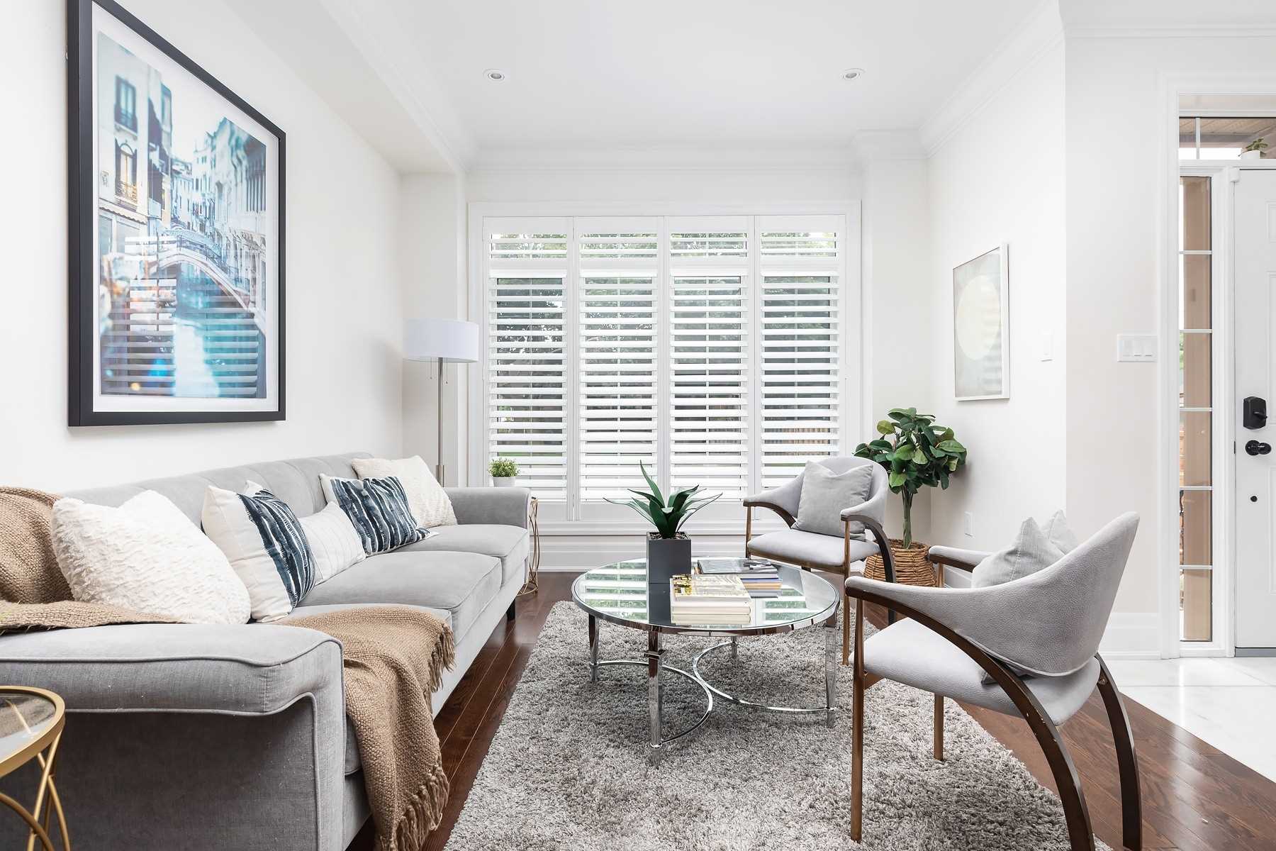 Bright living room with plantation shutters, grey sofa, armchairs, and hardwood floors
