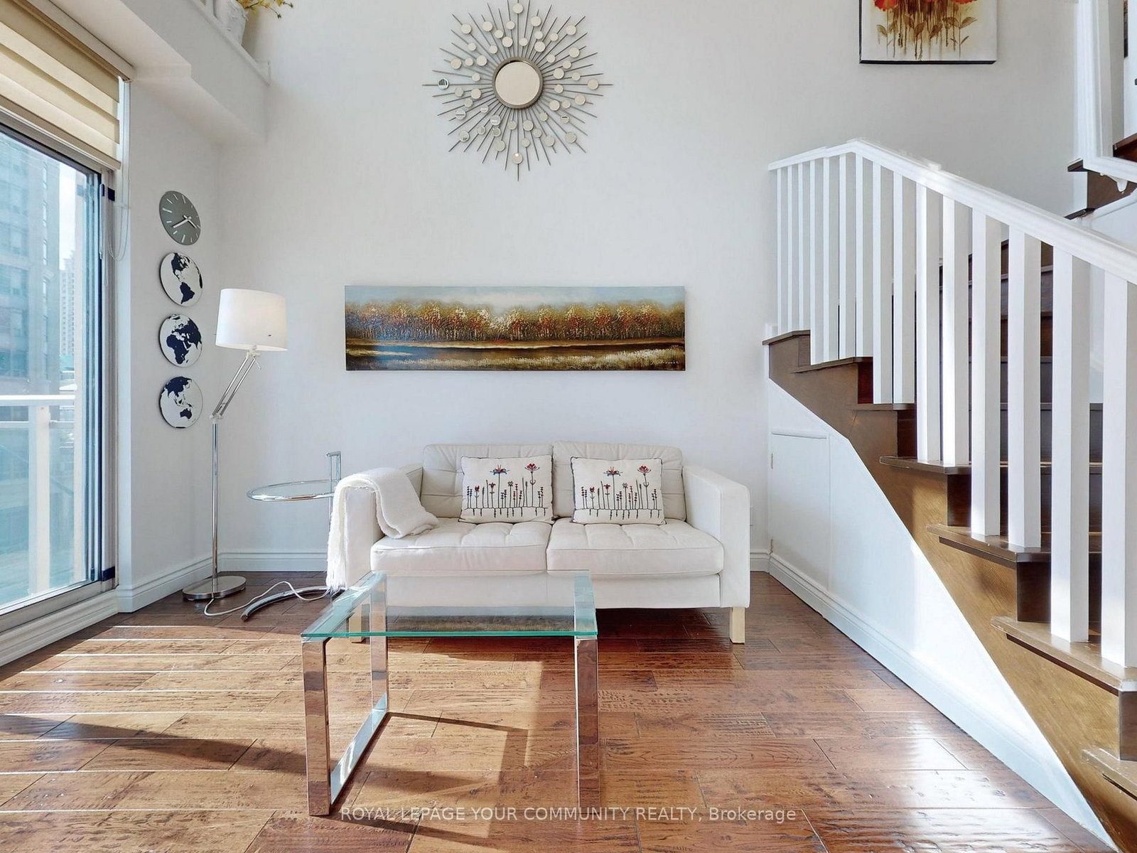 Double-height living room of the loft with a white sofa, sunburst mirror and the white staircase to the upper level