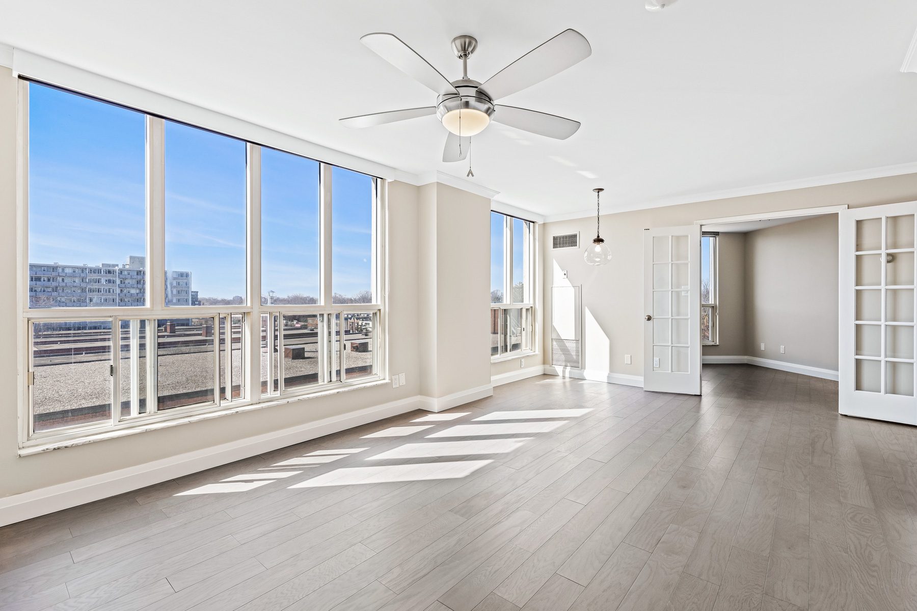 Bright living room of Suite 404 with walls of windows, a ceiling fan and French doors