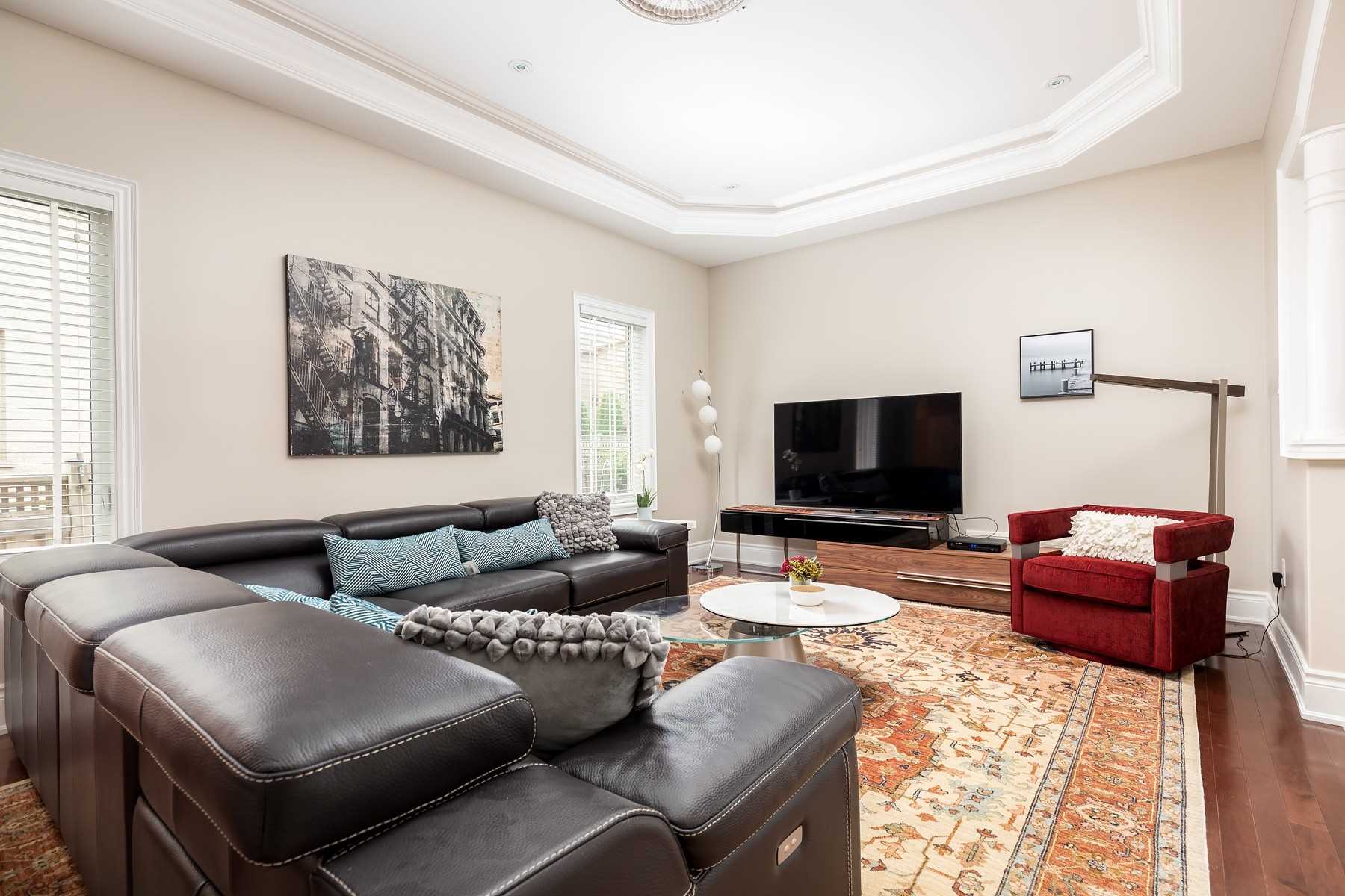 Living room of 33 Noce Way with a dark leather sectional, red armchair, and an octagonal tray ceiling