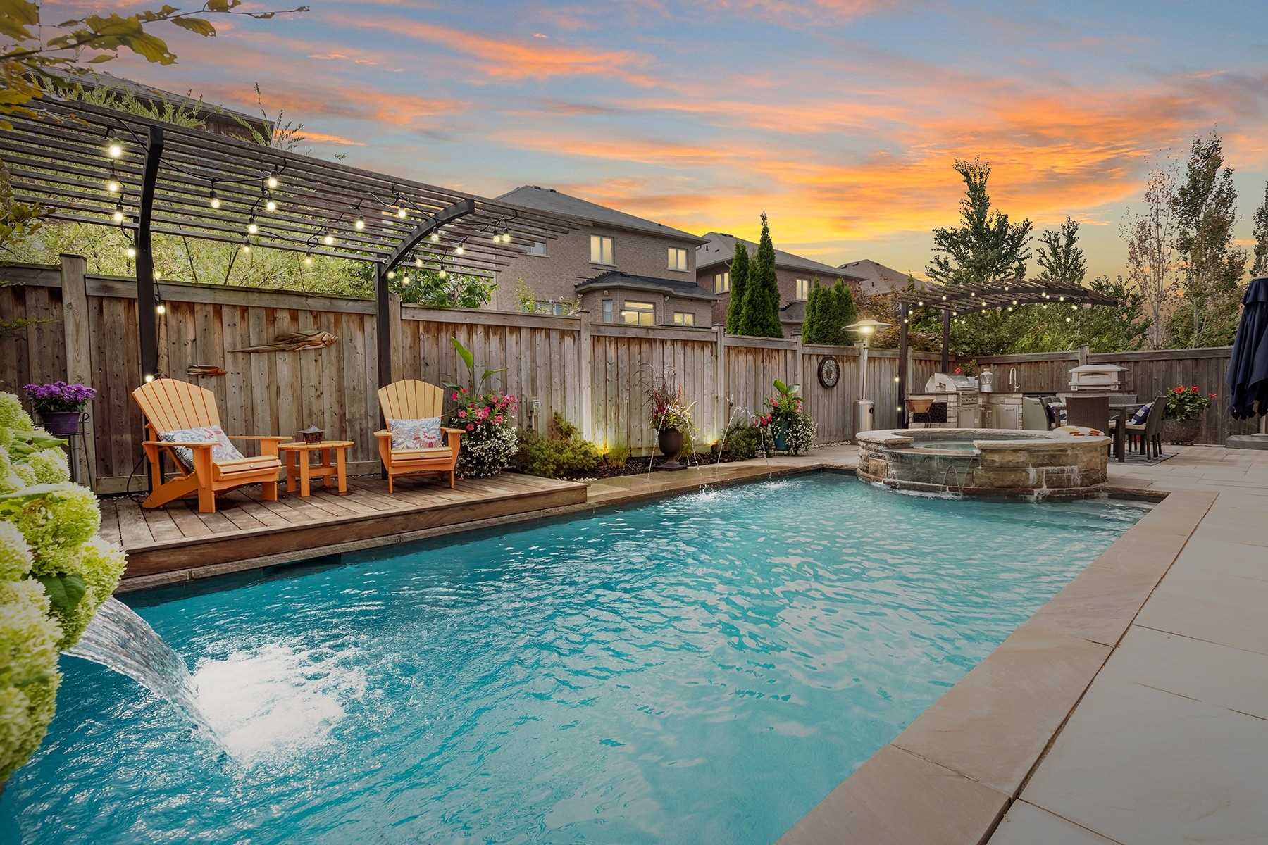 Backyard of 33 Noce Way at dusk — inground pool, stone spa, pergola with string lights, and an outdoor kitchen area