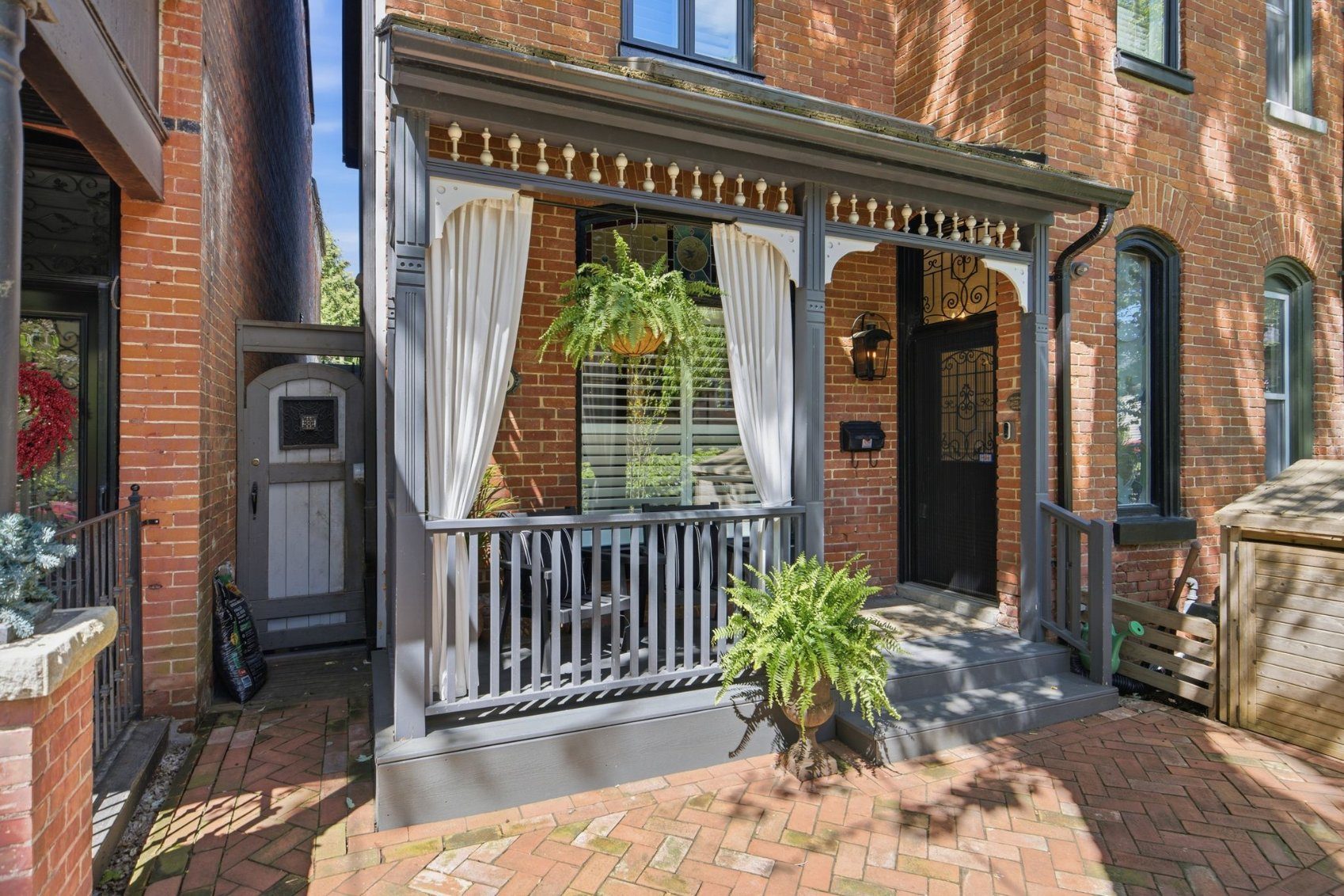 Victorian covered front porch at 336 Ontario Street with draped curtains, hanging ferns, and heritage brickwork