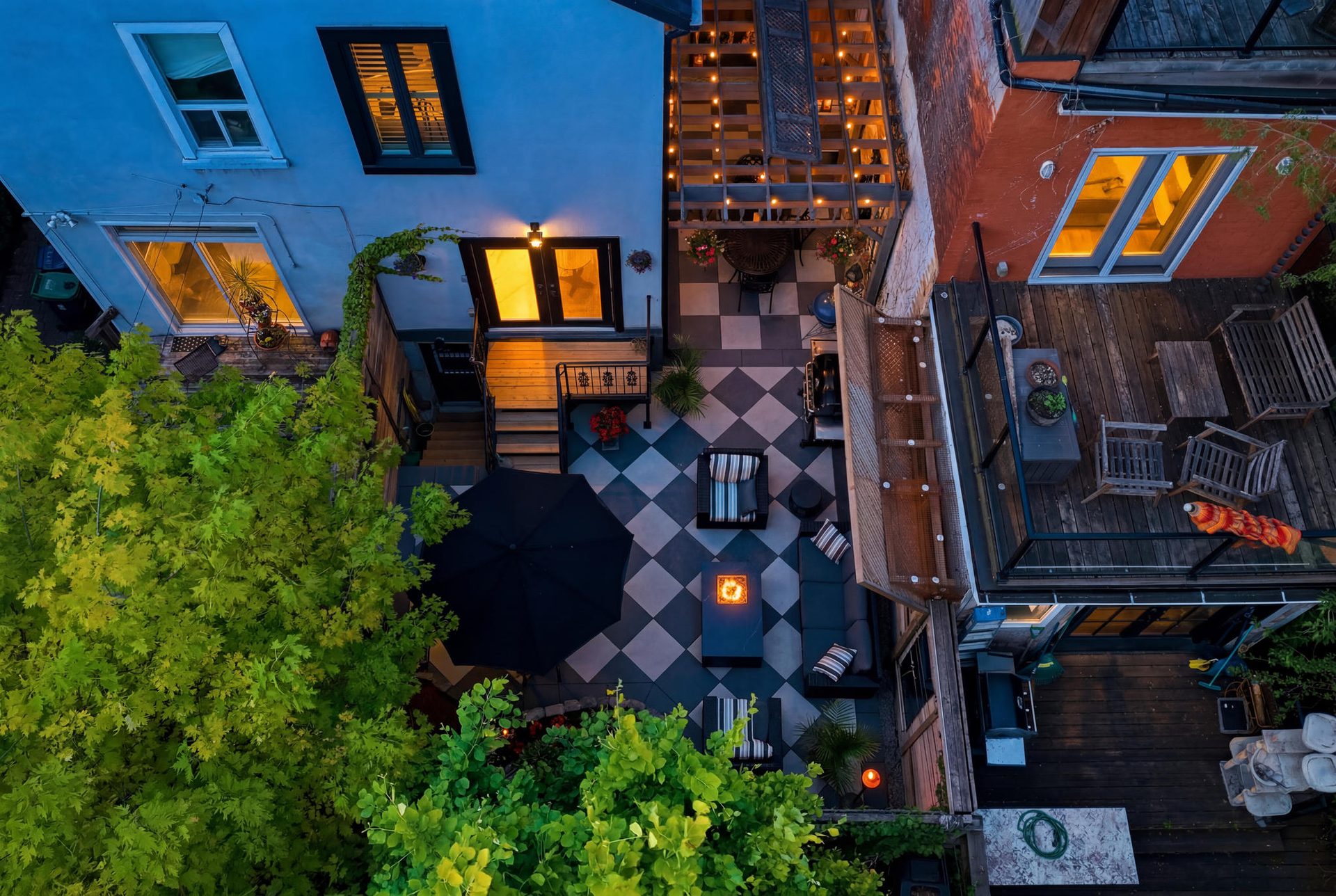 Aerial dusk view of the courtyard at 336 Ontario Street — checkerboard patio, glowing fire pit, lounge seating, and pergola strung with lights