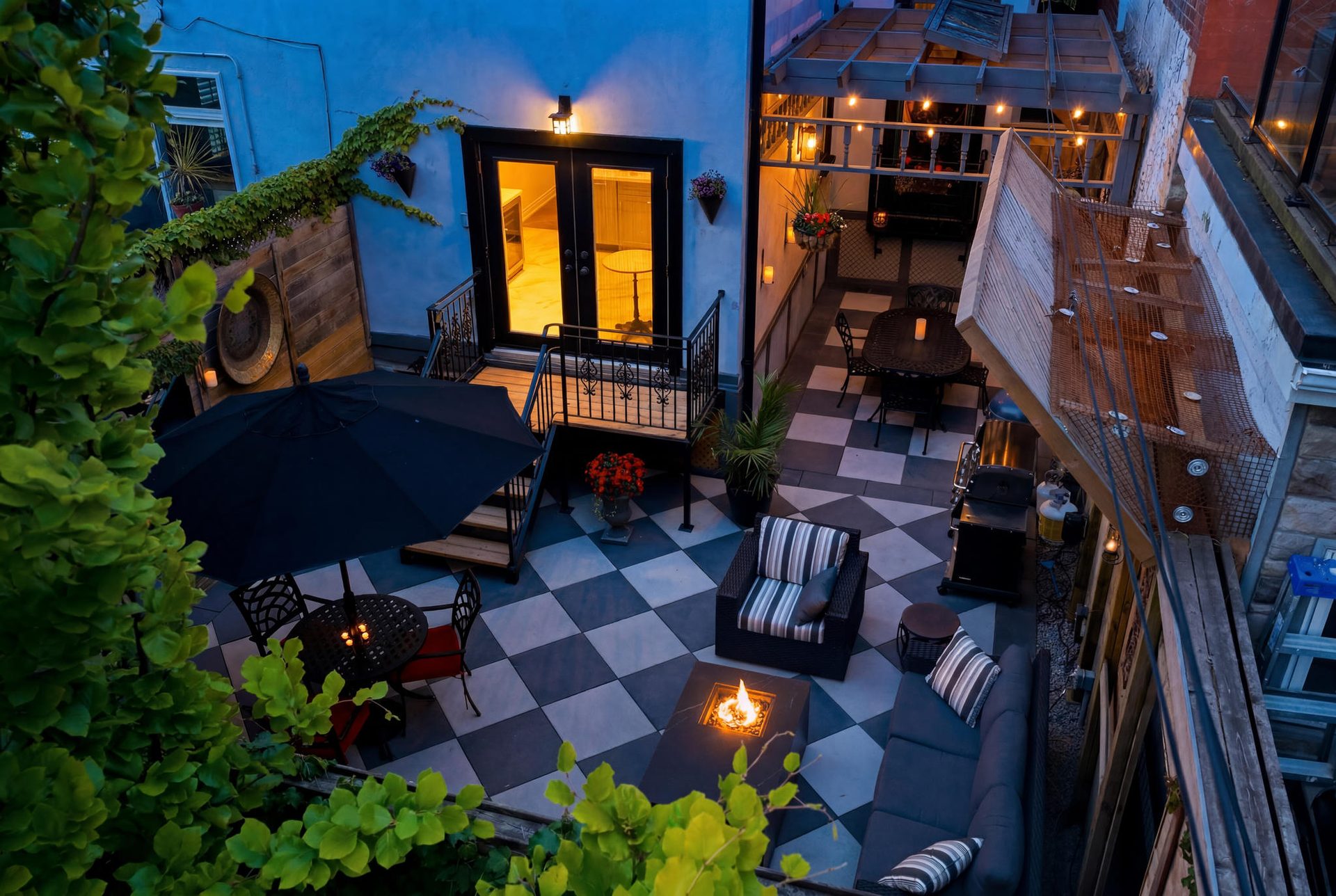 Twilight in the outdoor sanctuary at 336 Ontario Street — checkerboard patio with lit fire pit table, lounge chairs, glowing walk-out doors, and pergola with string lights