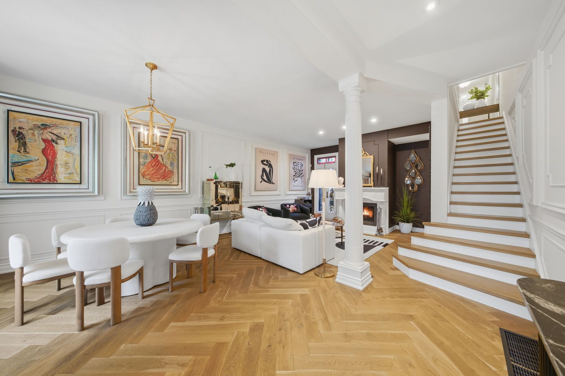 Open living and dining room with wood staircase, white fireplace, and herringbone hardwood floors