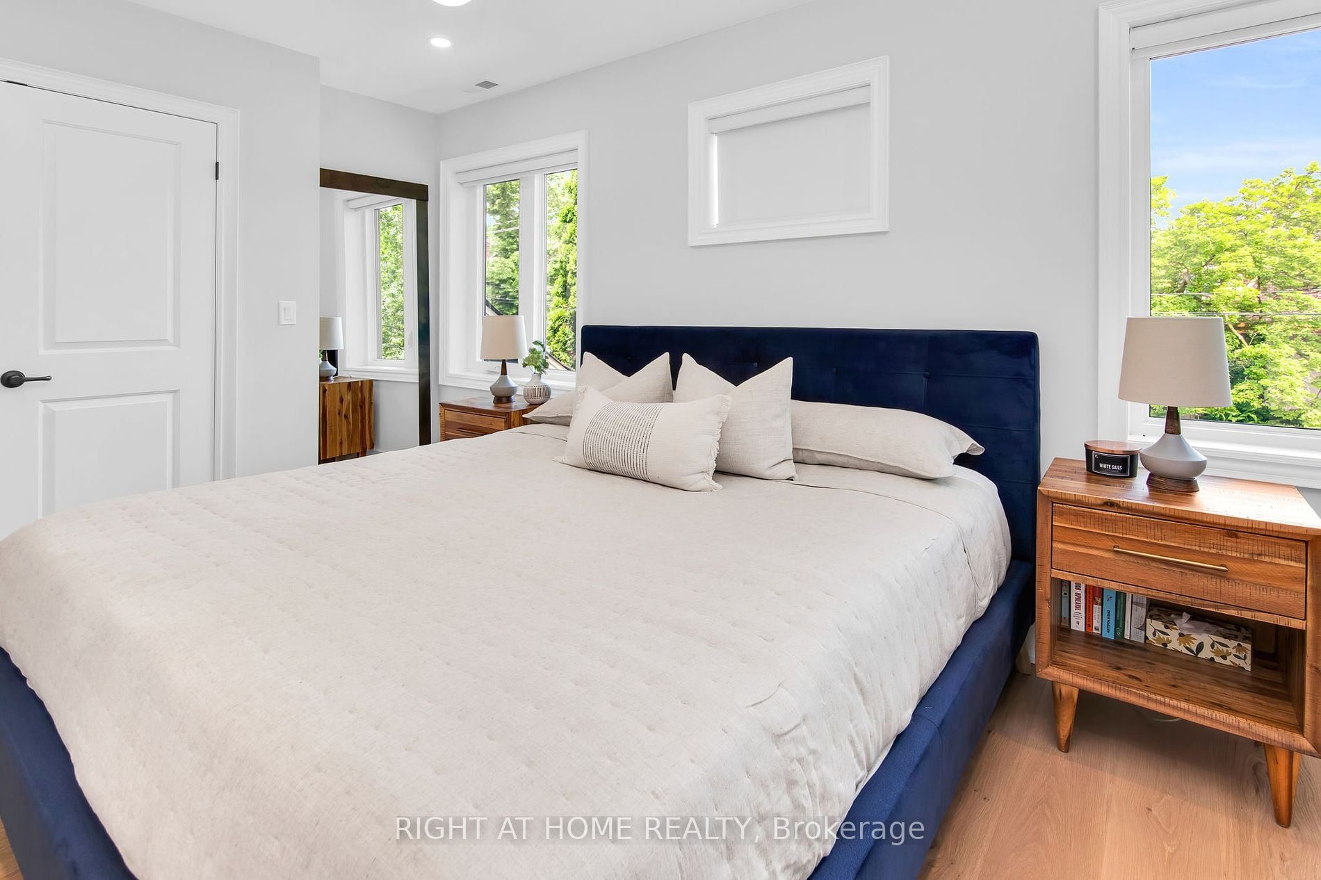 The primary bedroom at 39 Melrose Avenue — navy velvet headboard, white bedding and tree views from the new windows