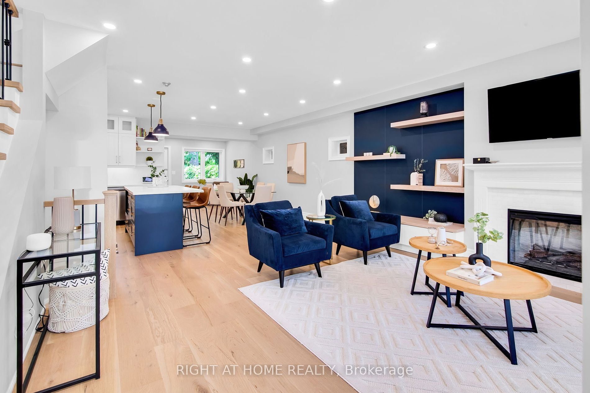 Open-concept main floor at 39 Melrose Avenue — custom kitchen with a navy island, dining area, and a navy accent wall with a gas fireplace and floating shelves