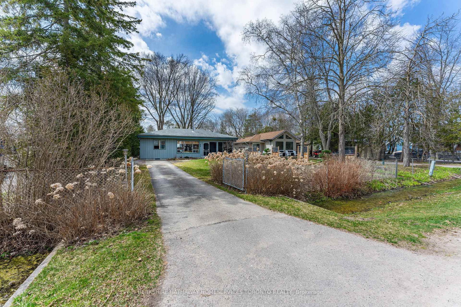 Front exterior of the classic lakeside bungalow at 62 Lakeshore Blvd, Innisfil, with paved driveway and mature trees
