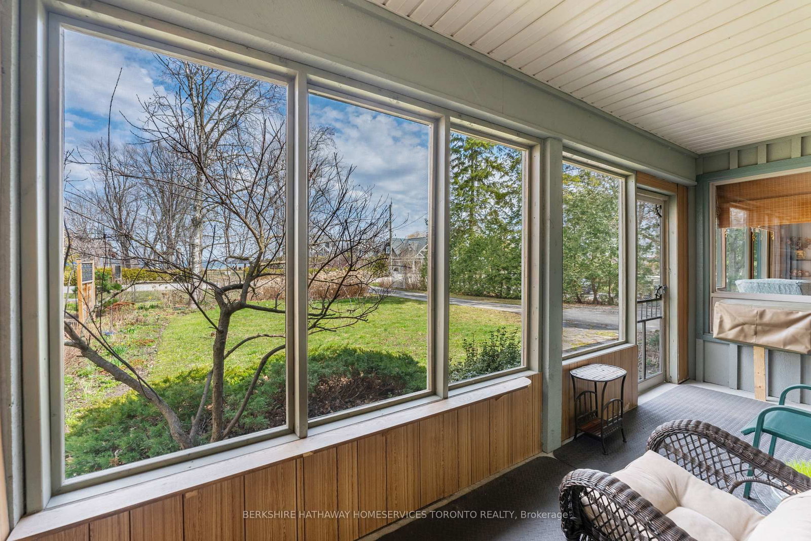 Screened sun porch with wicker seating and wall-to-wall windows overlooking the lawn
