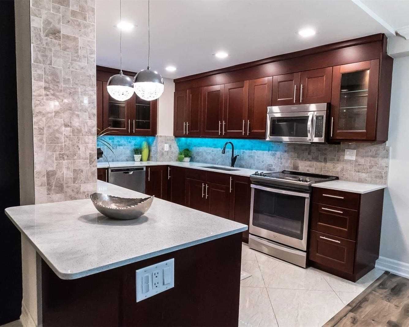 Renovated kitchen with dark wood cabinetry, quartz island, pendant lights and stainless steel appliances at 210 - 80 Inverlochy Blvd, Markham