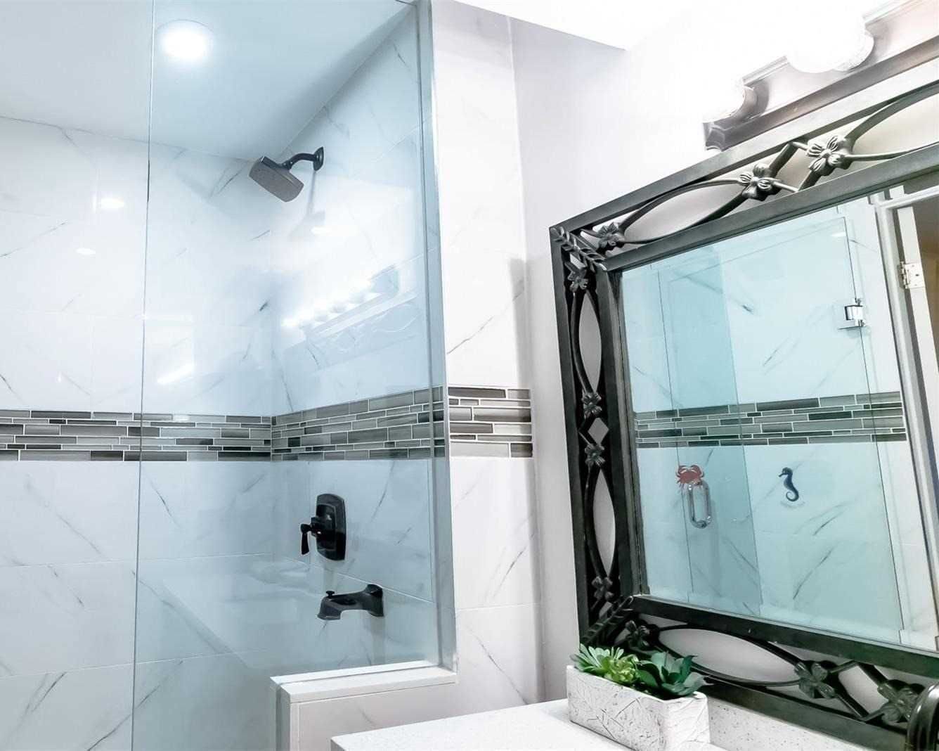 Renovated bathroom with glass shower, mosaic accent band and marble-look tile