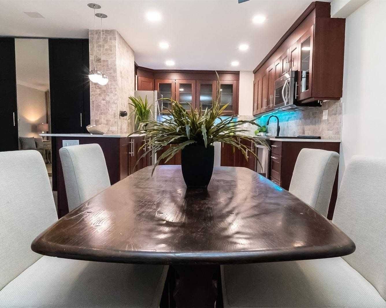 Dining table with the kitchen beyond, dark wood cabinetry and pendant lighting